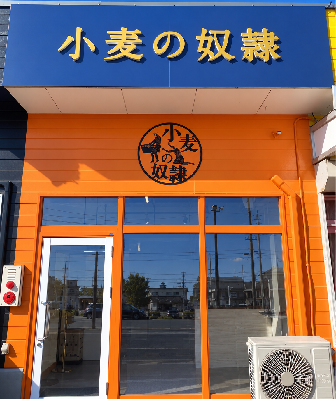 小麦の奴隷鹿屋店のオレンジ色の外観と青い看板