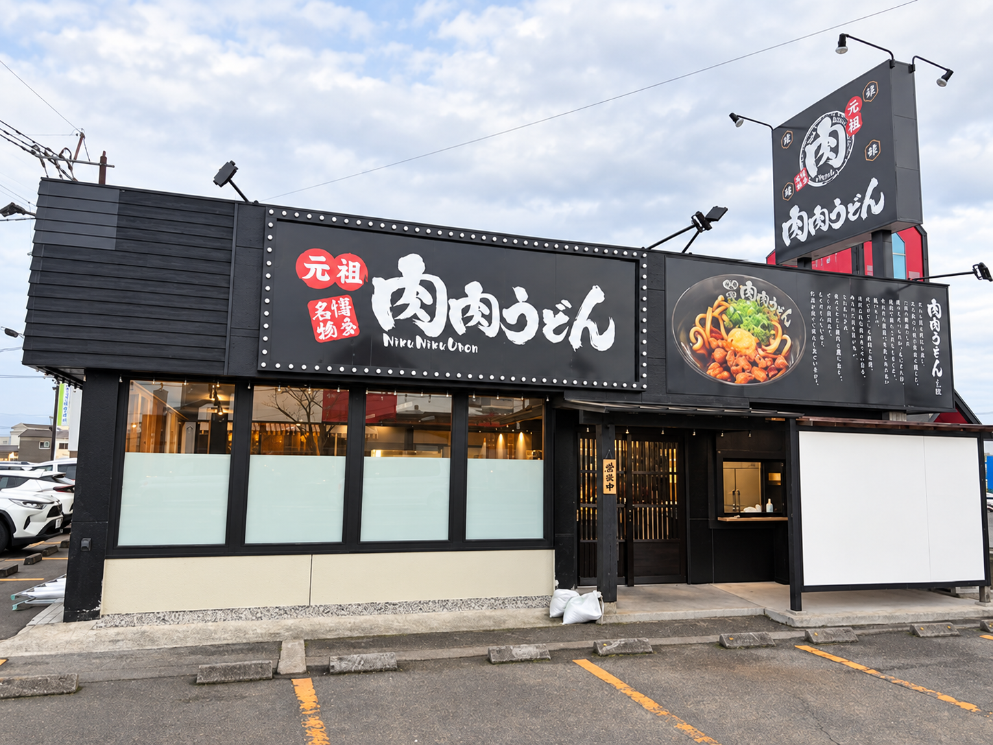 元祖肉肉うどん鹿屋店の外観。黒い看板と店舗入口。